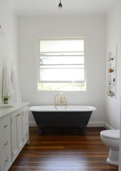 a white and black bath tub sitting in a bathroom next to a toilet on top of a hard wood floor