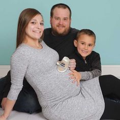 a man and woman pose for a photo while holding their son on the belly in front of a blue wall