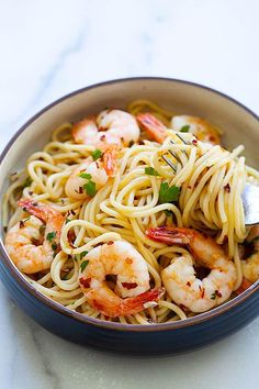 a bowl filled with pasta and shrimp on top of a white marble countertop next to a silver spoon