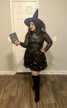 a woman wearing a witch costume and holding a book in her hand while standing next to a door