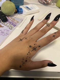 a woman's hand with black nail polish and stars on the ring finger tattoo