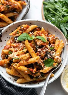 two bowls filled with pasta and spinach on top of a white table next to other dishes