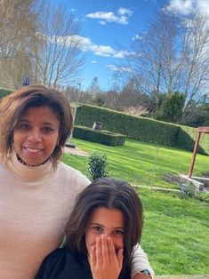 two women standing next to each other in front of a lush green park with trees