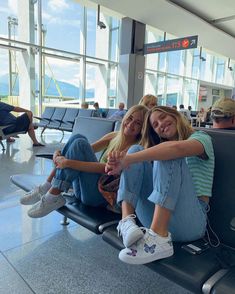 two young women sitting on the back of an airport luggage cart smiling at the camera