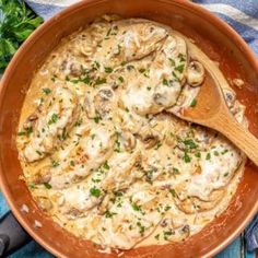 a pan filled with mushrooms and sauce on top of a blue cloth next to a wooden spoon