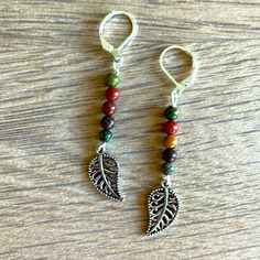 two pairs of earrings with beads and leaves hanging from them on a wooden table top