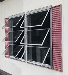 an open window on the side of a building with red shutters and metal bars