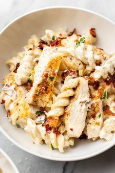 a white bowl filled with pasta covered in chicken and cheese sauce on top of a marble table