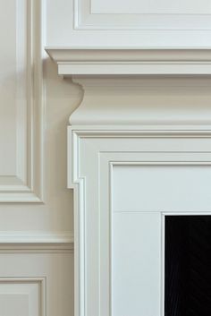 the corner of a room with white painted walls and trimmings on the fireplace