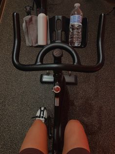 the legs of a person on a stationary bike with water bottles and other items around them