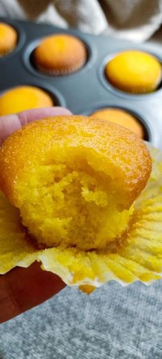 a person holding up a muffin in front of some cupcakes inside a muffin tin