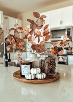 a wooden tray topped with lots of white pumpkins and pineconi next to a glass jar filled with candles