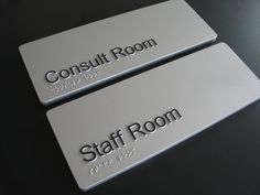 two silver business cards sitting on top of a black table with the words consult room and staff room