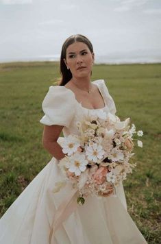 a woman in a wedding dress holding a bouquet of flowers and posing for the camera