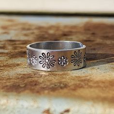 If you love flowers and/or being outdoors, this ring is perfect for you! Daisy flowers in two sizes adorn this hand crafted adjustable (midi) ring. I personally hand stamp all of the lettering and designs in my studio. Each design is hand aligned and punched into the metal, so the placement of the wording and designs will vary slightly from piece to piece. After stamping, I darken the impressions so they stand out. To retain the contrast, it is highly recommended that the piece is not exposed to Personalized Silver Adjustable Flower Ring, Adjustable Nickel-free Flower Ring For Promise, Adjustable Nickel-free Flower Promise Ring, Flower Shaped Engraved Adjustable Promise Ring, Adjustable Flower Engraved Promise Ring, Adjustable Stamped Flower Jewelry, Handmade Adjustable Flower Ring For Anniversary, Handmade Adjustable Engraved Ring For Everyday, Adjustable Hand Stamped Midi Rings