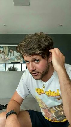 a man sitting on top of a bed next to a wall with pictures on it