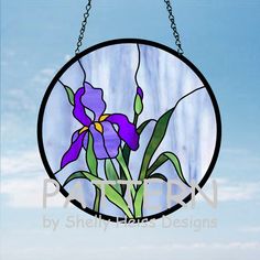 a round stained glass window with purple flowers hanging from it's chain on a blue sky background