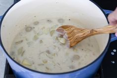 a wooden spoon in a blue pot filled with soup on top of a gas stove