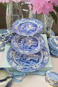 a blue and white china set on a table with pink flowers in a vase behind it