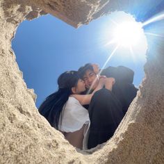 two people standing in the sand with their arms around each other