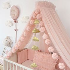 a pink crib with pom poms hanging from it's sides and a canopy over the crib