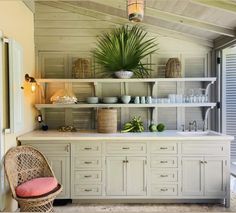 a kitchen with white cabinets and shelves filled with dishes on top of each shelf next to a potted plant