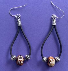 the earrings are decorated with silver and brown beads on black leather cords, which hang from sterling - plated earwires