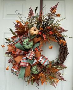 a wreath with pumpkins and leaves hanging on a door