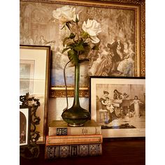 a vase filled with white flowers sitting on top of a table next to books and framed pictures