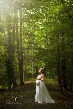 a woman standing in the middle of a forest wearing a white dress and posing for a photo