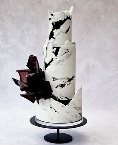 a three tiered cake with black and white icing on a metal stand in front of a gray background