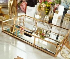 a gold tray filled with cosmetics and perfume bottles on top of a white countertop