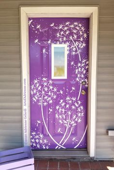 a purple front door with white flowers painted on it and a bench next to it