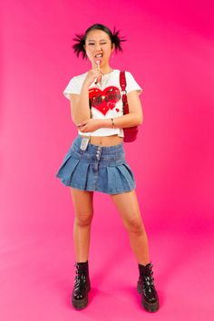 a young woman posing with her tongue out in front of a pink background wearing a white shirt and denim skirt