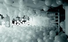 black and white photograph of balloons hanging from the ceiling in a room with ladders