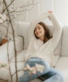 a woman sitting on top of a white couch next to a vase filled with flowers