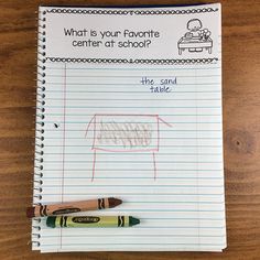 a notebook with writing on it and two crayons in front of the page