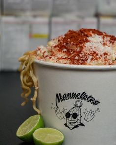 a cup filled with noodles and sauce next to lime wedges on a black table