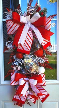 a red and white christmas wreath with candy canes, bells and ornaments hanging on the front door