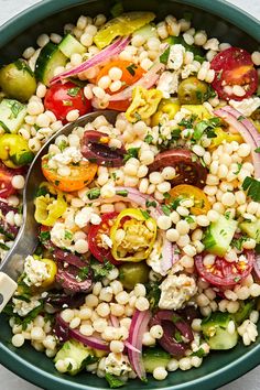 a bowl filled with corn, tomatoes, cucumbers and other vegetables next to a spoon