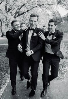 three men in tuxedos are walking down the sidewalk and one is holding his arm around another man's neck