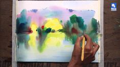 a person is holding a paintbrush and drawing on a piece of paper with watercolors