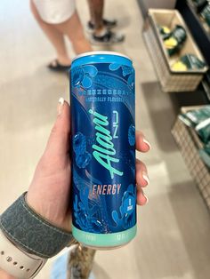 a person holding up a can of energy drink in a store aisle with other people