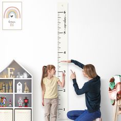 a woman and girl are measuring the height of a tall growth chart in a child's room