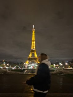 a man standing in front of the eiffel tower at night with his back turned to the camera