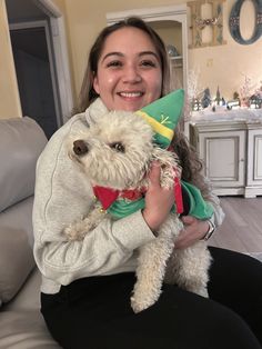 a woman sitting on a couch holding a dog wearing a gnome hat and green sweater