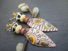 These earrings feature tribal enameled copper charms by Verreetcuivre in France. The leaf shaped charms are decorated with a sun motif set against a cream and black zebra striped background. Above the charms are mauve coconut wood beads followed by gold disc beads. Next are cream coconut wood beads. These support tribal lamp-work glass beads, also by Verreetcuivre. The lamp-work beads are black with white stripes on the bottom and orange with aqua raised glass dots on top. Bi-cone brass beads to Bohemian Enamel Earrings Nickel Free, Bohemian Enamel Earrings Nickel-free, Nickel-free Bohemian Enamel Earrings, Bohemian Hand-painted Copper Jewelry, Hand Painted Bohemian Enamel Jewelry, Bohemian Hand Painted Copper Jewelry, Bohemian Hand-painted Enamel Jewelry, Bohemian Hand Painted Enamel Jewelry, Hand Painted Copper Bohemian Earrings