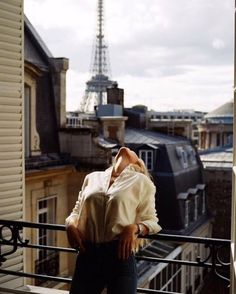 a woman standing on top of a balcony next to a building with the eiffel tower in the background