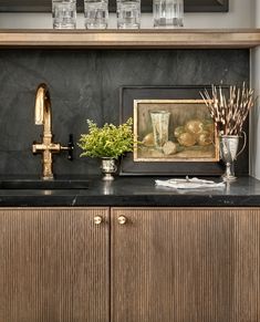 a black counter top with vases and plants on it next to a framed painting