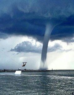 a boat is in the water with a large tornado coming out of it's back